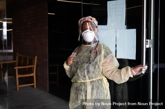 Nurse with PPE and stethoscope holding door of medical building open