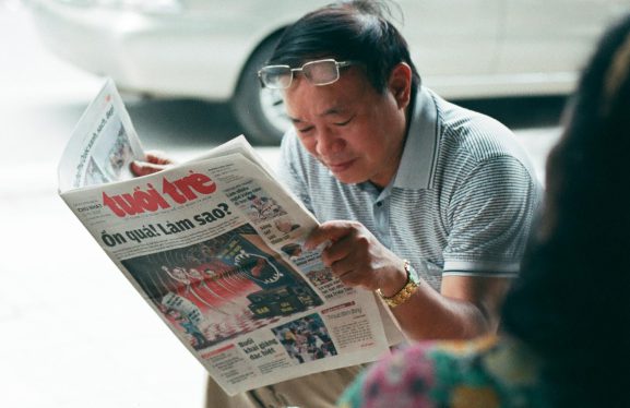 Man with glasses reading Vietnamese newspaper